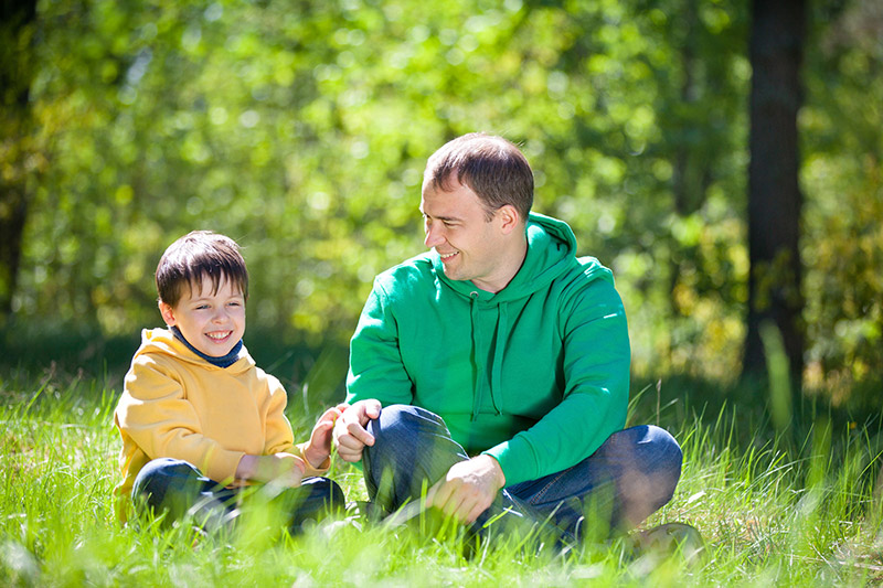 Father and Young Son Talk Outside on Grass